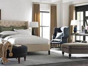 a large bedroom with brown curtains, an open window, a blue armchair, a gray chair, and a stool with cushion