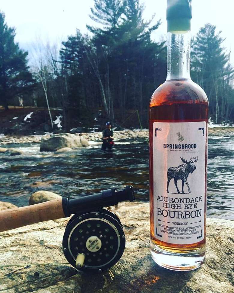 a bottle of adirondack high rye bourbon on a rock in front of a river