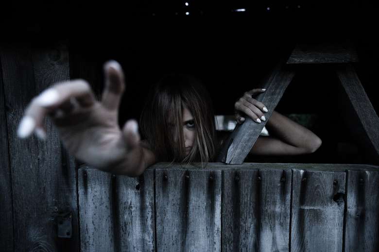 creepy woman reaching from behind wooden wall