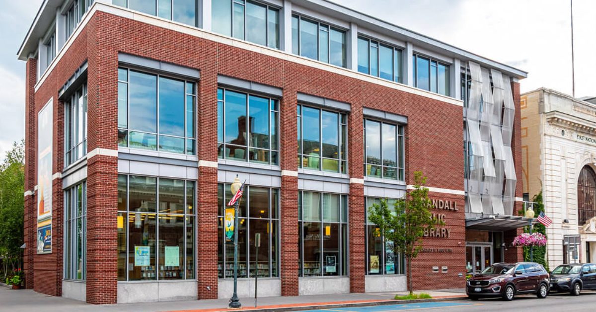 Brick building with windows from top to bottom with two cars out front