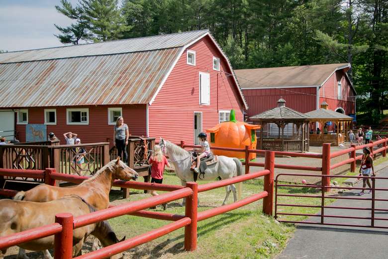 A pair of red barns with horses in front