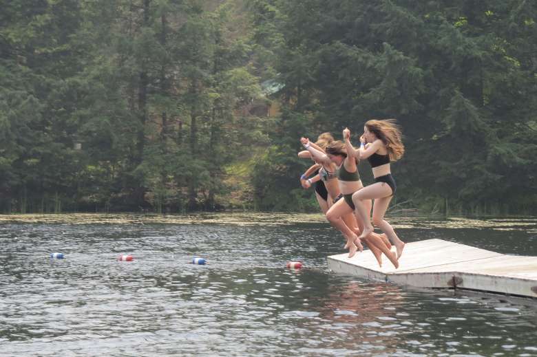 kids jump off a dock into the water holding hands