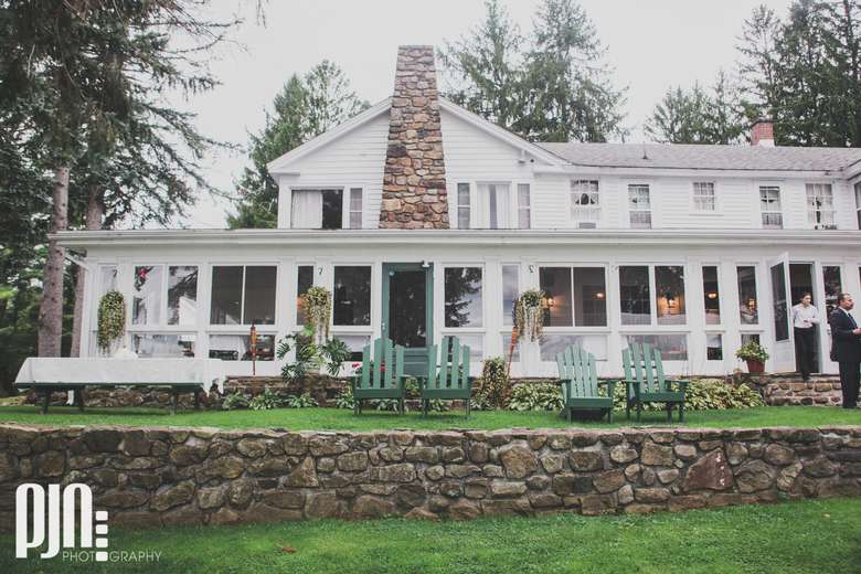 A white building with a porch and a stone wall in front