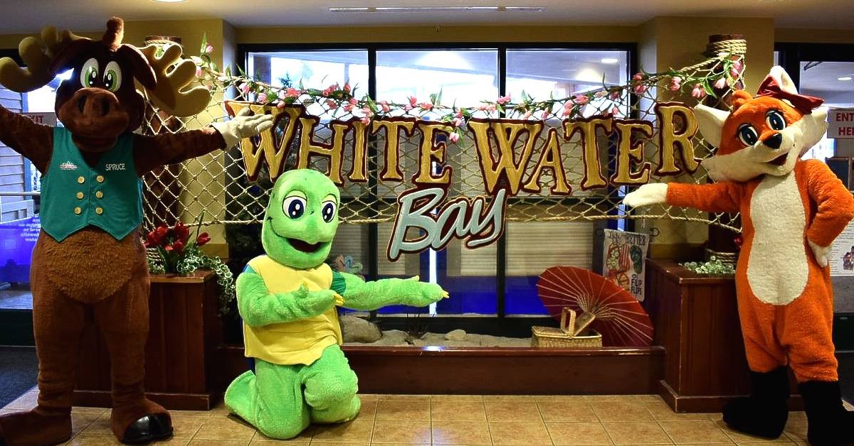 costumed people pose by white water bay sign