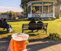 beer held up in front of gazebo with people in park
